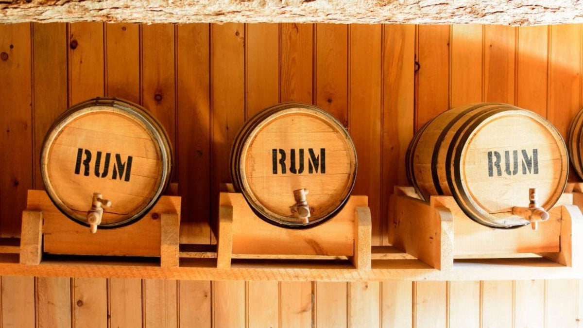 Three wooden rum barrels marked “RUM” lined up against a wooden wall.