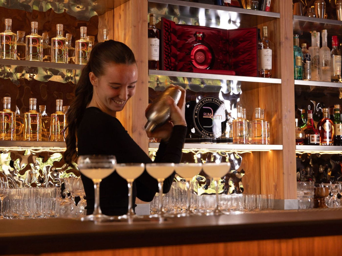 Anya Garrow shakes cocktails behind the bar with five coupe glasses in front of her