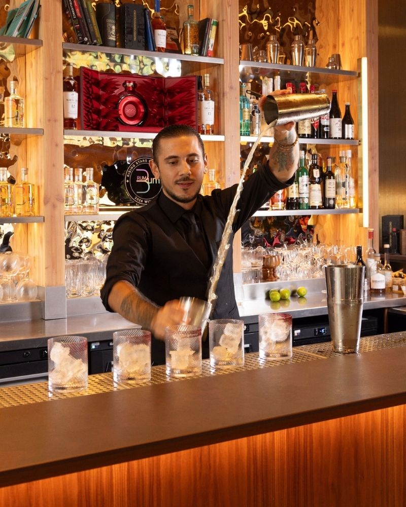 Rising Stars finalist pours a drink between glasses of ice behind the bar