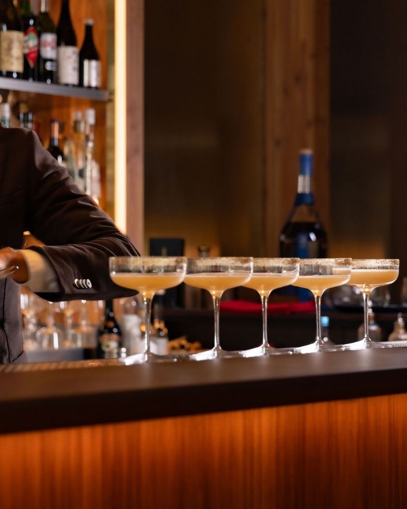 Five pale cocktails in coupe glasses lined up on the bar