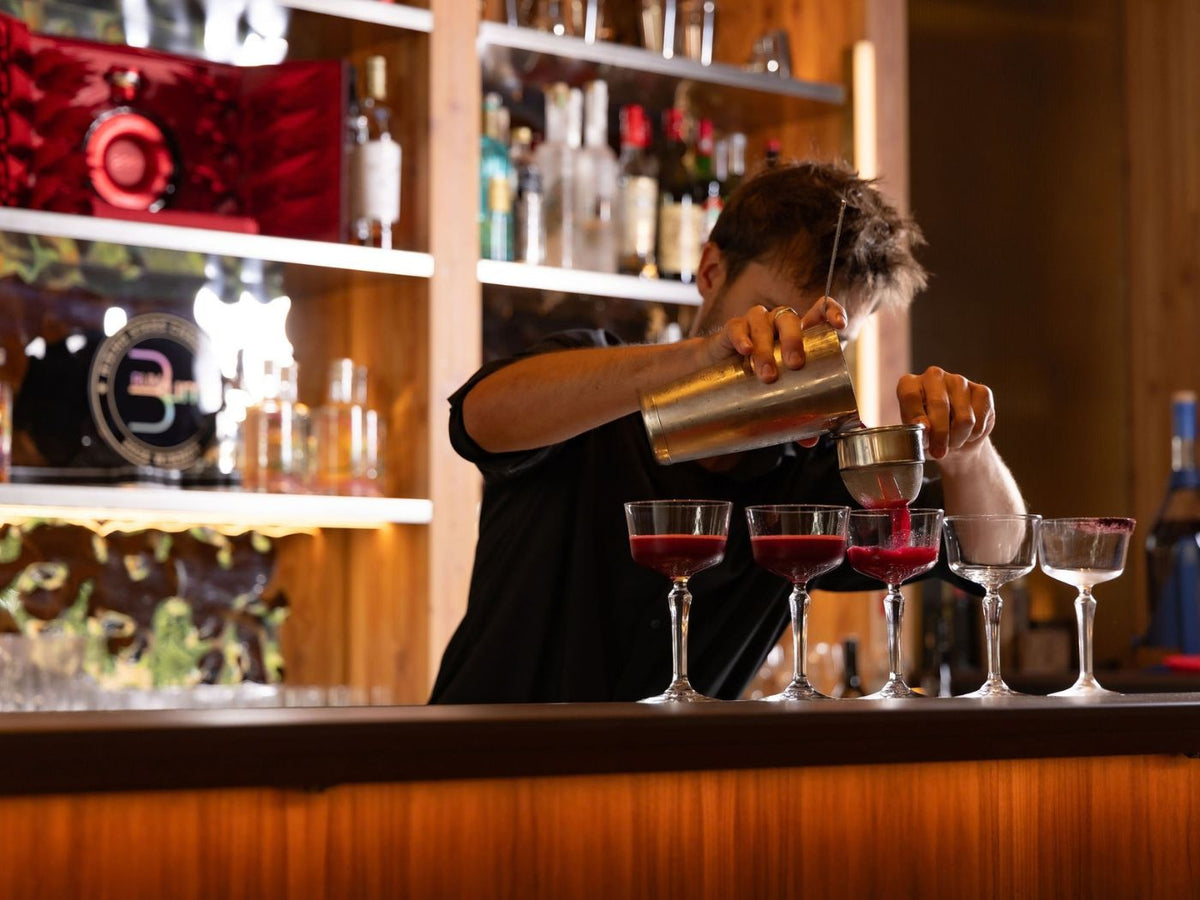 Rising Stars finalist strains red cocktails into a row of coupe glasses