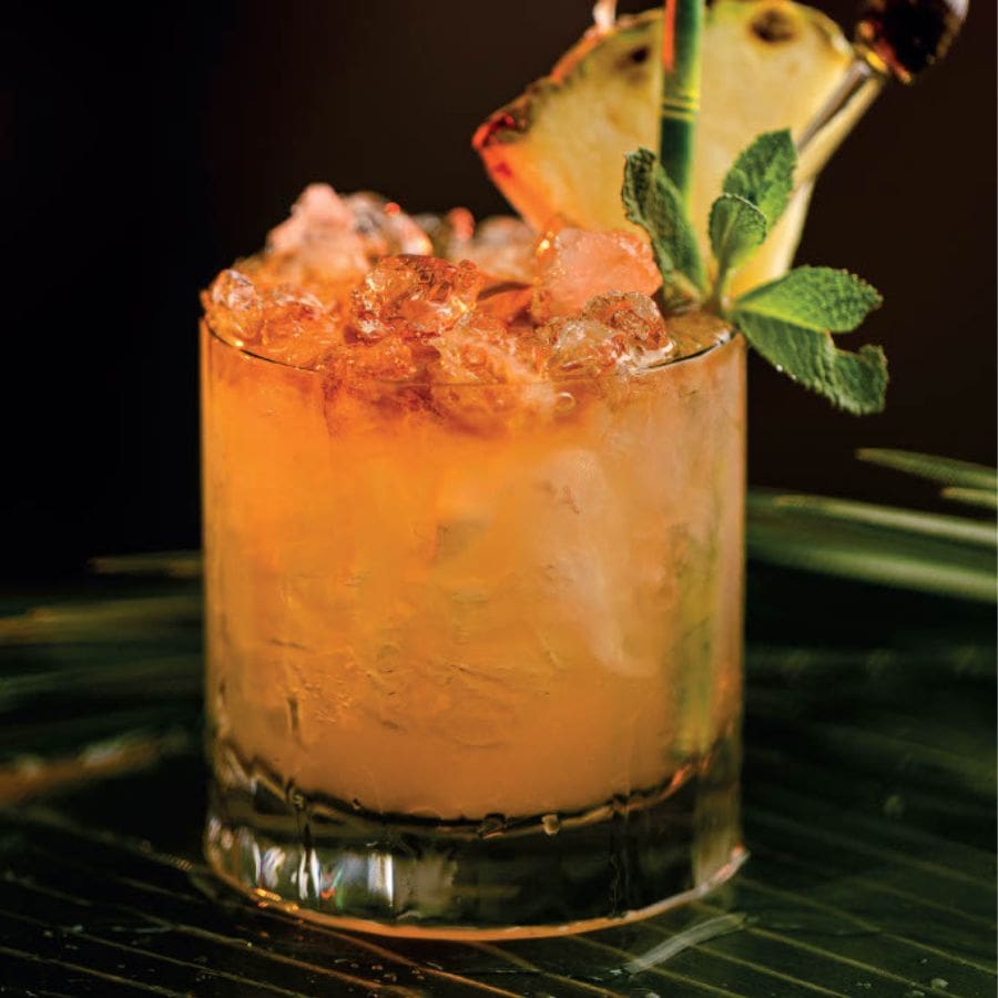 Tropical mai tai cocktail with crushed ice, pineapple slice, and mint garnish.