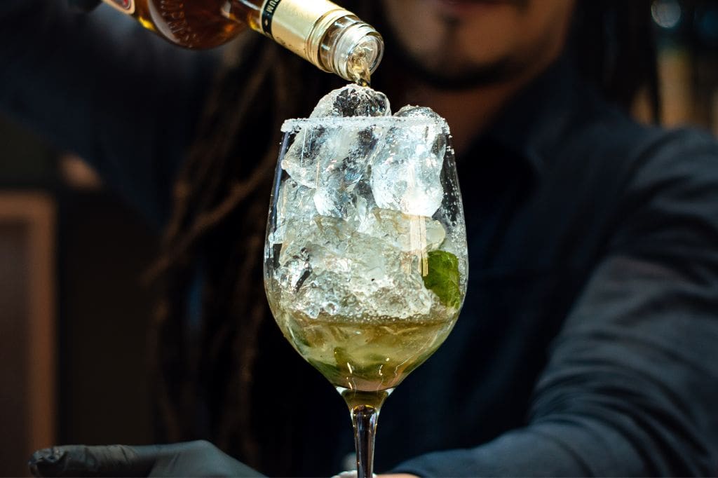 Bartender pouring Rum into a glass filled with ice and mint.