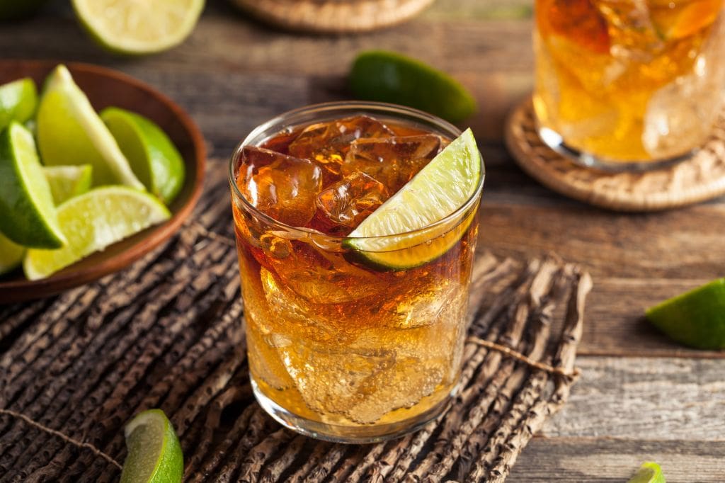Glass of dark rum cocktail with lime wedge on a rustic wooden table. Dark & Stormy