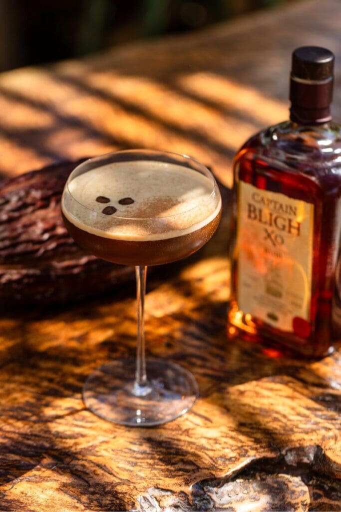 Espresso martini style whos going nuts rum cocktail garnished with coffee beans on a wooden surface beside a bottle of Captain Bligh XO aged rum.