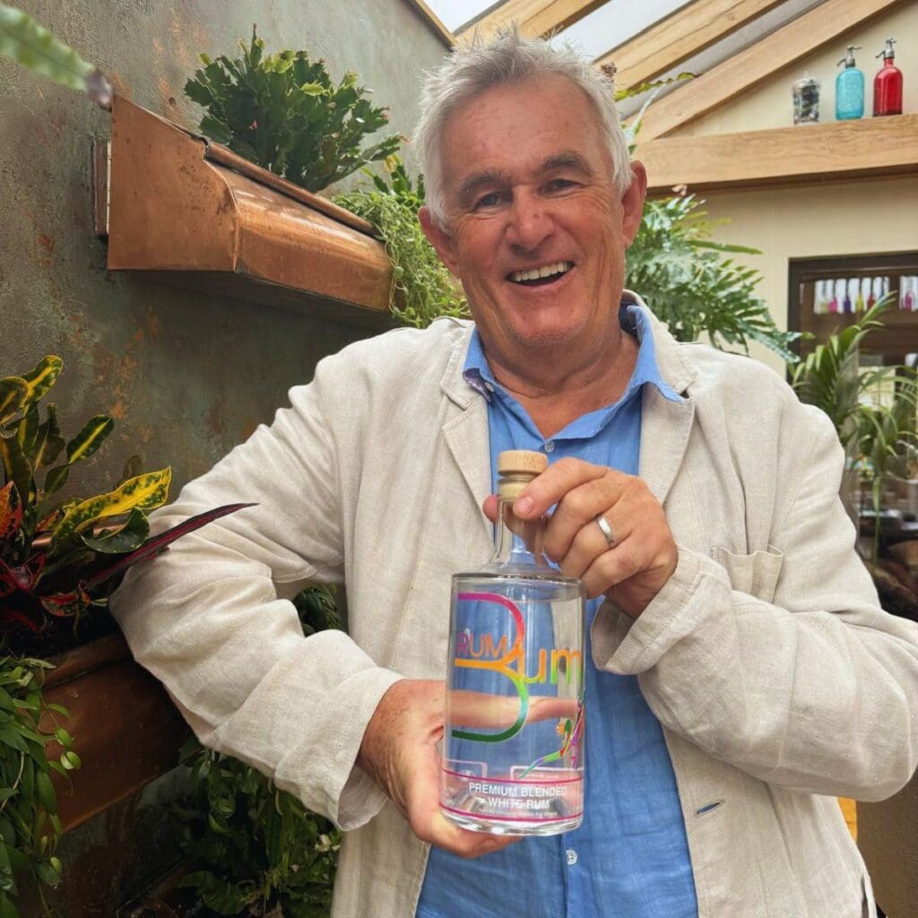 Smiling man holding a bottle of white rum in a bright indoor garden setting, illustrating what does rum taste like.